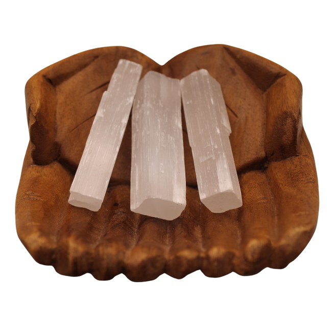 Three selenite sticks placed on a textured wooden surface.